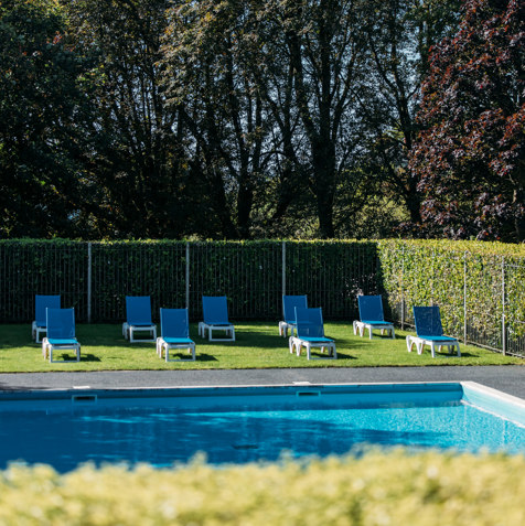 A sunny grass terrace beside a heated outdoor pool with sun loungers