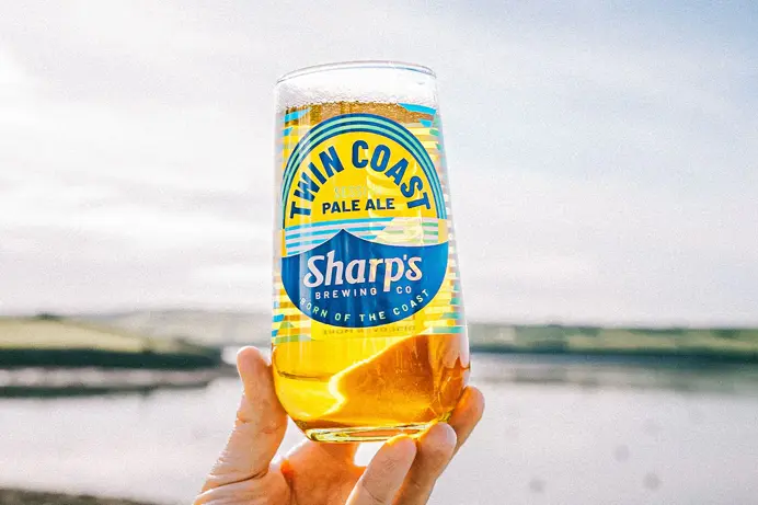 A pint of pale ale being held by a hand with a scenic view in background