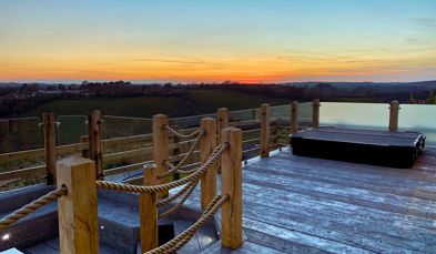 External of a luxury lodge decking with sunken fire pit, sunken hot tub and countryside views at sunset
