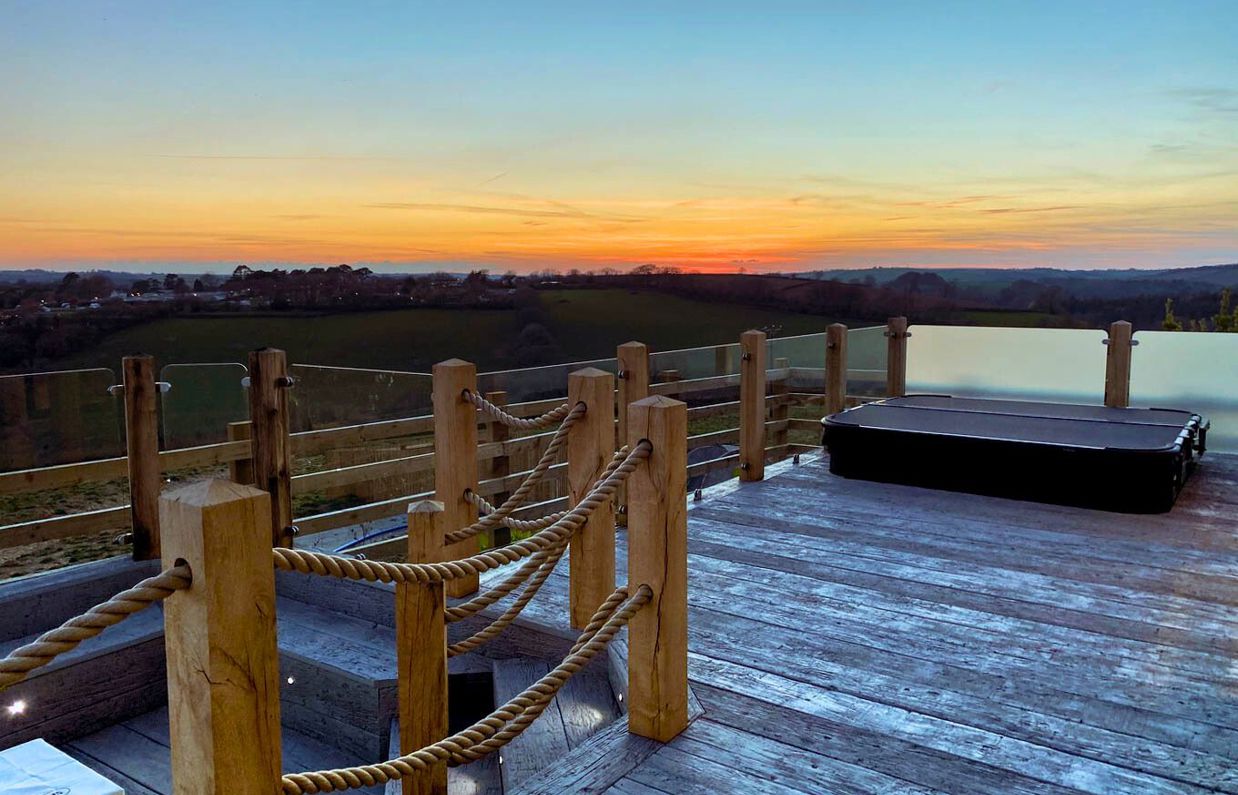 External of a luxury lodge decking with sunken fire pit, sunken hot tub and countryside views at sunset