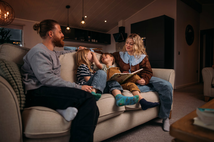 A family of four sat on the sofa of a lodge reading a children's book together