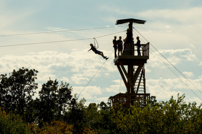 A group of people on a zipline podium with one going down the wire