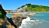 Looe beach, pier and harbour at the bottom of a green hill with blue sea waters