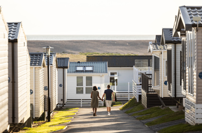 Couple walking down lane at Chesil Beach Holiday Park with Chesil Beach in background