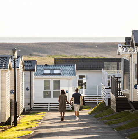 Couple walking down lane at Chesil Beach Holiday Park with Chesil Beach in background