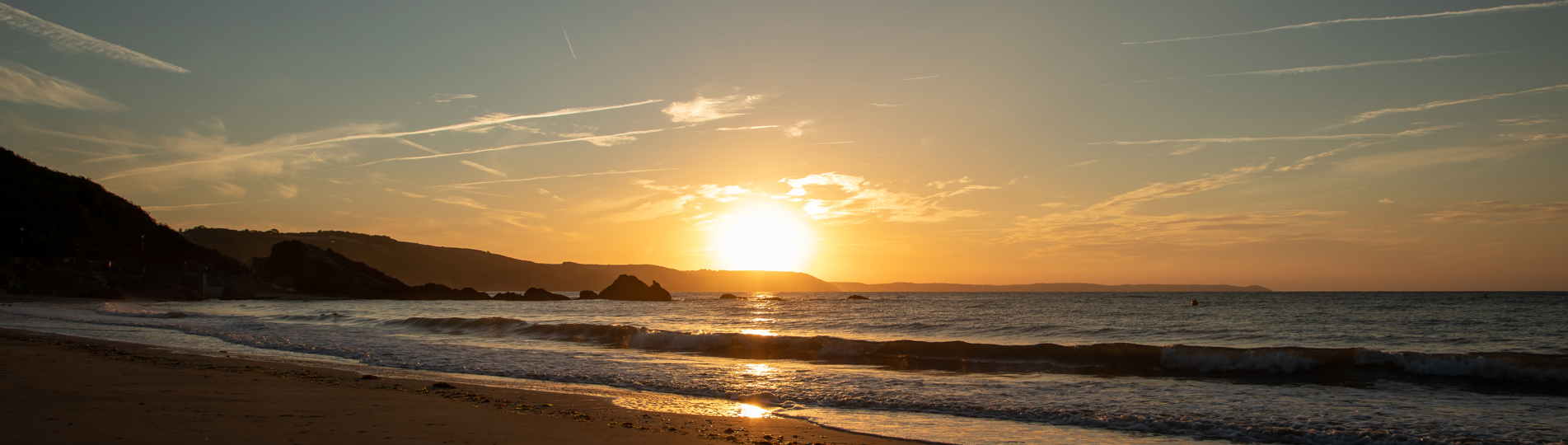 A large stretch of beach at sunrise with rocky cliffs in the background and calm waters