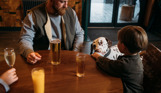 A man and a young boy at an indoor table with a black and white dalmatian dog with the young boy feeding the dog ice cream
