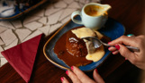 A sticky toffee pudding dessert with custard and sauce being cut into with a spoon
