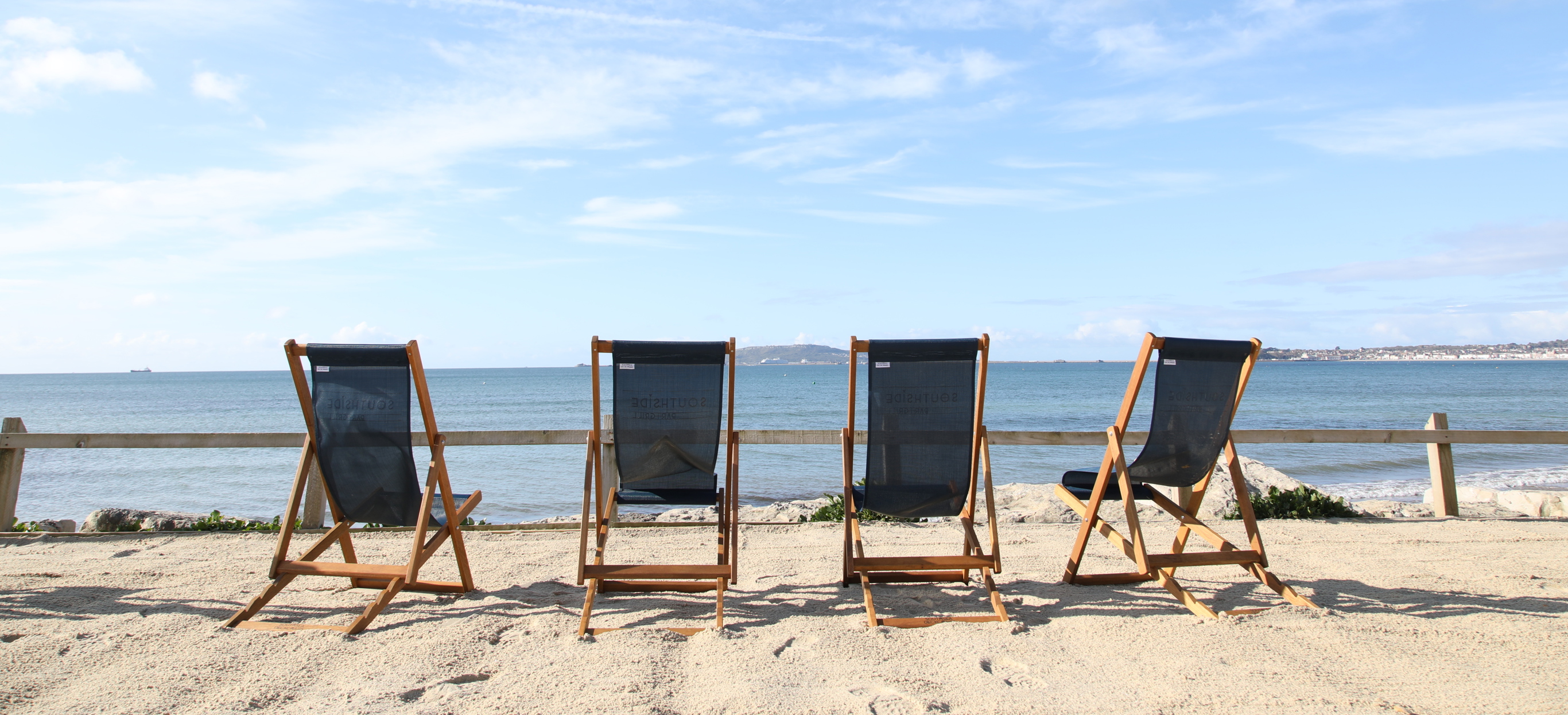 Deckchairs sat on the sand at Southside area overlooking the sea with blue skies