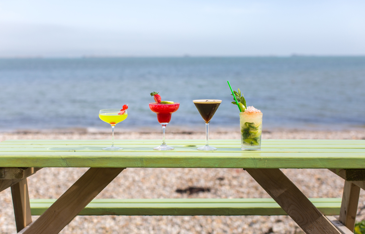 Four cocktails on an outdoor bench looking out to sea