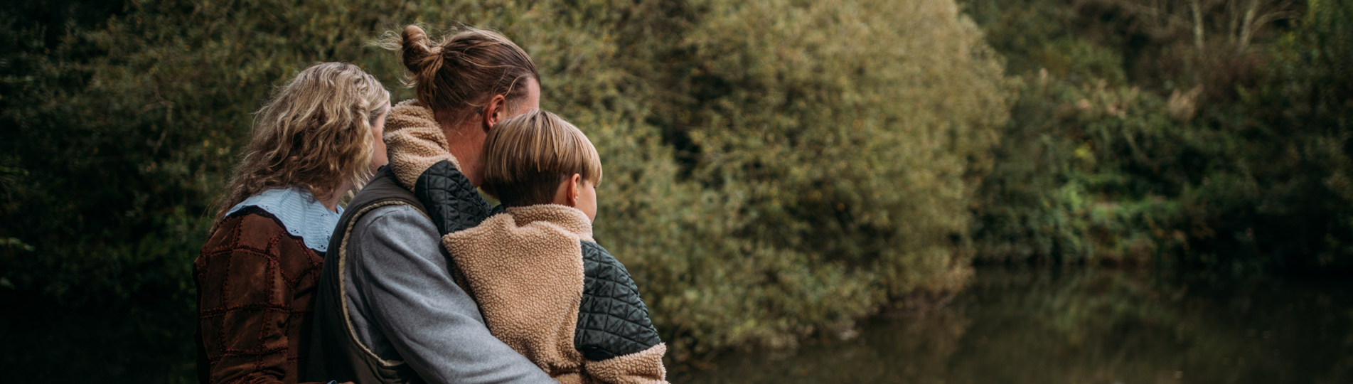 A family of three from behind among trees and lake