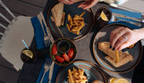 A selection of different filled baguettes with chips, salad and drink on a table taken from above with hands picking up the food