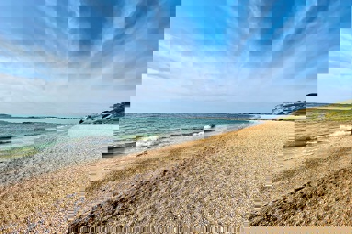 A shingle beach with calm sea and views of Portland and Weymouth Bay on a sunny blue sky day