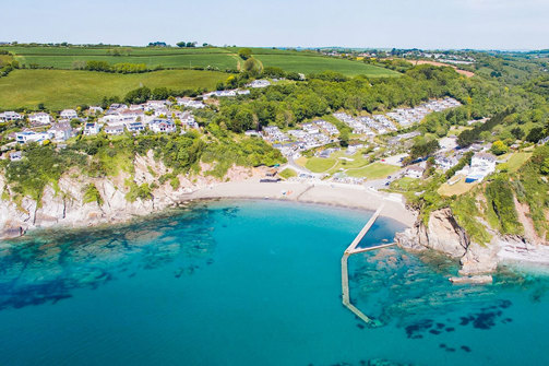 A small sandy bay at the bottom of rolling countryside hills with bright blue water
