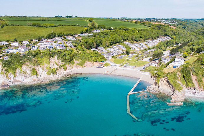 A small sandy bay at the bottom of rolling countryside hills with bright blue water