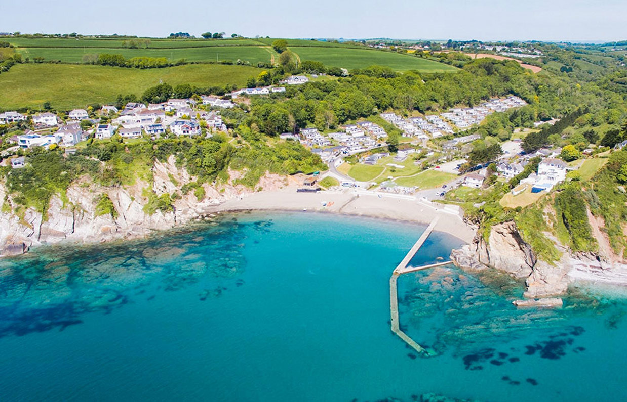 A small sandy bay at the bottom of rolling countryside hills with bright blue water