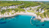 A small sandy bay at the bottom of rolling countryside hills with bright blue water