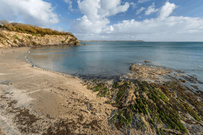A sandy beach with rocky areas by the sea surrounded by headland