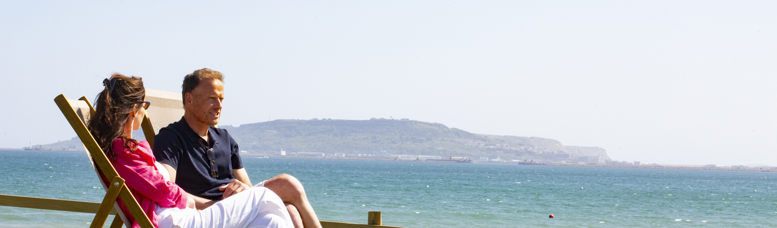 Couple relax on deckchairs overlooking Weymouth beach