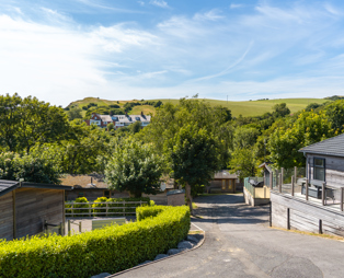 An area of a lodge park surrounded by rolling countryside hills, woodland, trees and holiday lodges