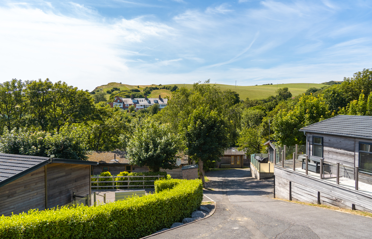 An area of a lodge park surrounded by rolling countryside hills, woodland, trees and holiday lodges