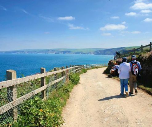 A couple walking on a coastal path with views of the sea and rolling hills