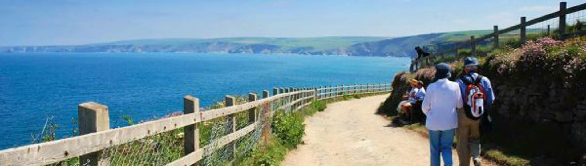 A couple walking on a coastal path with views of the sea and rolling hills
