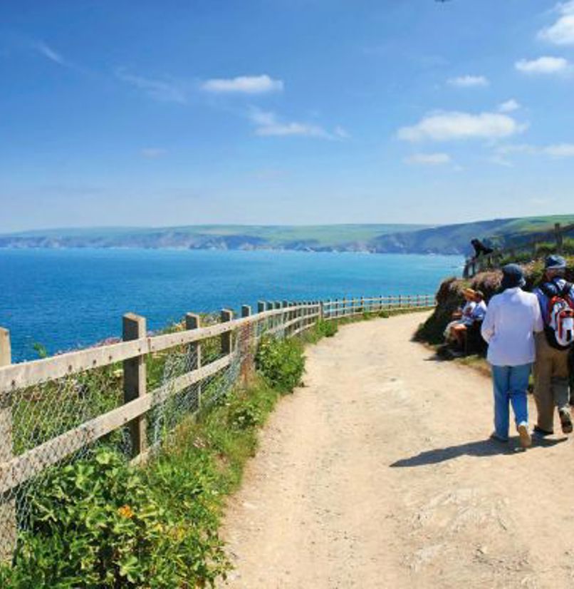 A couple walking on a coastal path with views of the sea and rolling hills