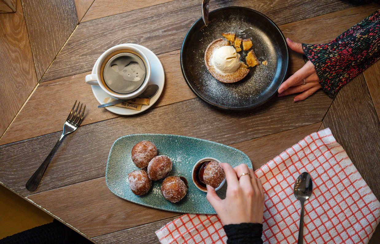 A plate of mini donuts with chocolate sauce and another plate of pastry with ice cream and a coffee taken from above
