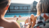 A young girl and boy in an outdoor pool with a mum and dad sat on sun loungers in the sun