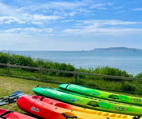 A range of kayaks sat in a field by the sea