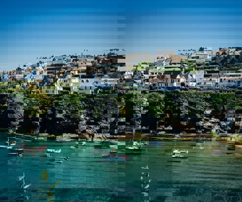 A quaint, quiet Cornish harbour with boats and houses atop the hill