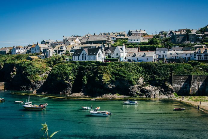 A quaint, quiet Cornish harbour with boats and houses atop the hill