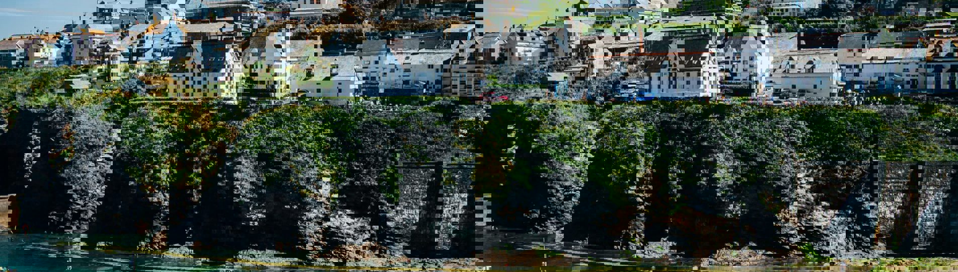 A quaint, quiet Cornish harbour with boats and houses atop the hill