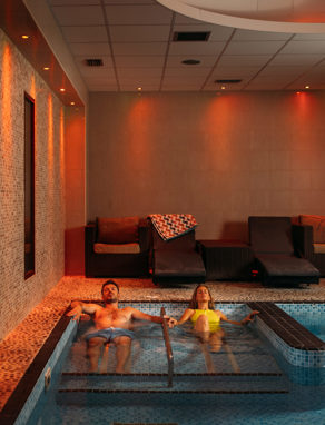 A Couple Relaxing in a Spa Pool with Loungers and Calm Lighting