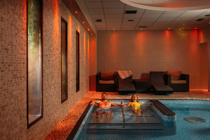 A Couple Relaxing in a Spa Pool with Loungers and Calm Lighting