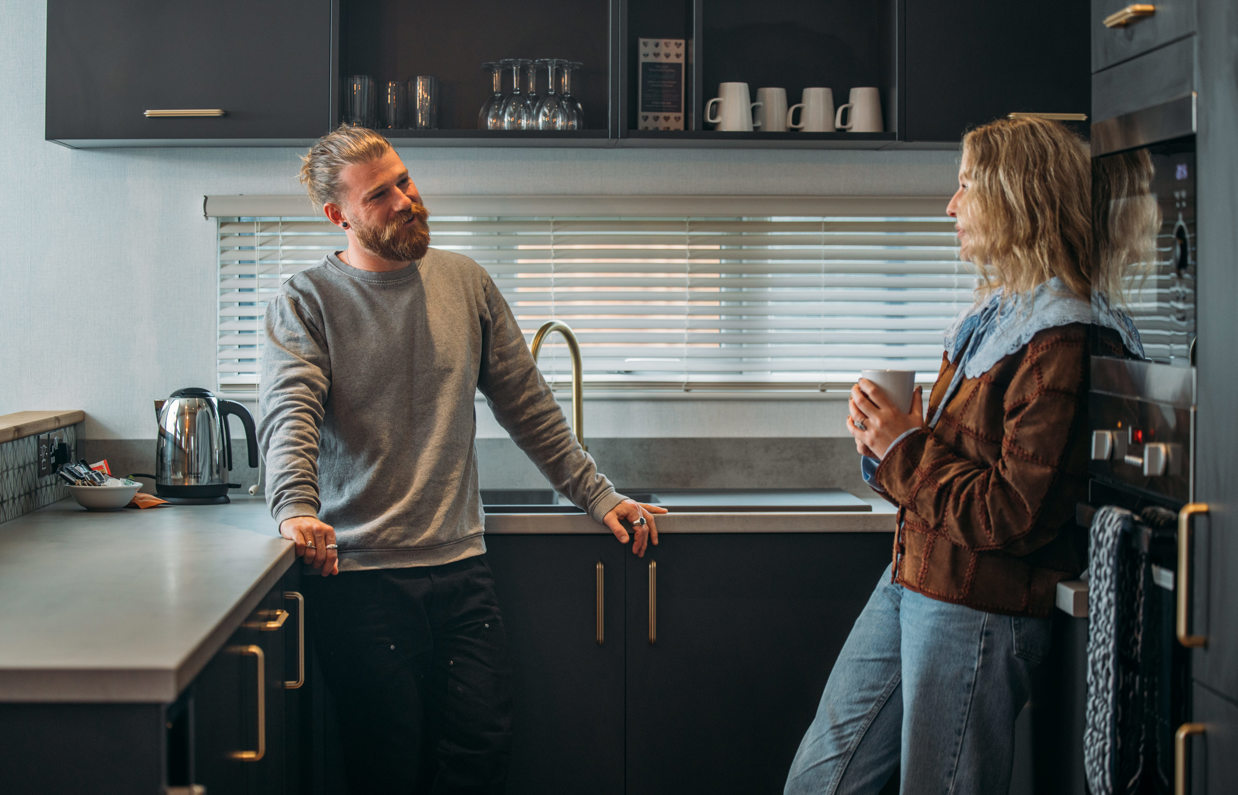 A couple standing in the kitchen of a luxury lodge at Tregoad Holiday Park smiling at each other