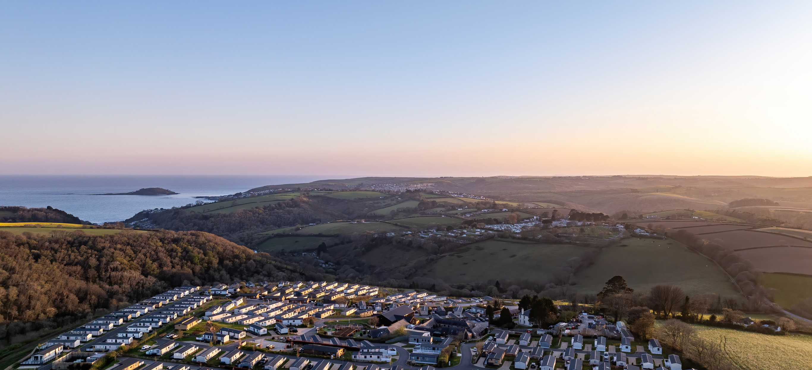 An aerial view of Tregoad Holiday Park looking out towards the sea and Looe Island at sunset