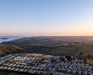An aerial view of Tregoad Holiday Park looking out towards the sea and Looe Island at sunset
