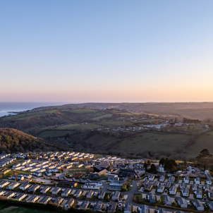 An aerial view of Tregoad Holiday Park looking out towards the sea and Looe Island at sunset