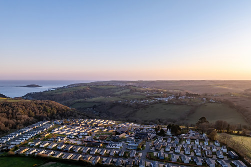 An aerial view of Tregoad Holiday Park looking out towards the sea and Looe Island at sunset