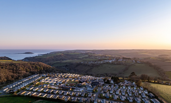 An aerial view of Tregoad Holiday Park looking out towards the sea and Looe Island at sunset