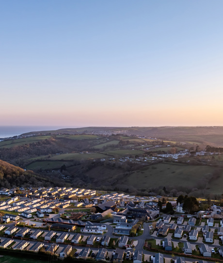 An aerial view of Tregoad Holiday Park looking out towards the sea and Looe Island at sunset