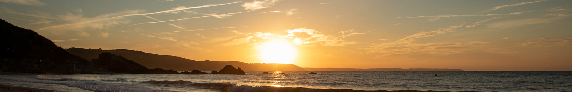 A large stretch of beach at sunrise with rocky cliffs in the background and calm waters