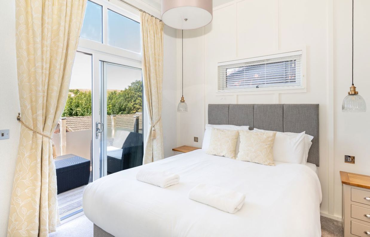 Internal of a lodge master bedroom with sliding doors out to decking with outdoor furniture