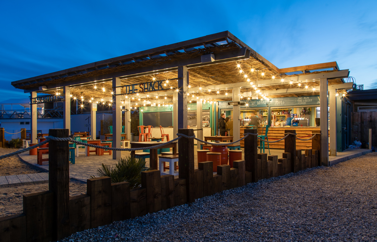 An outdoor beach bar and street food shack at night with fairy lights and outdoor seating by the sea