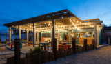 An outdoor beach bar and street food shack at night with fairy lights and outdoor seating by the sea