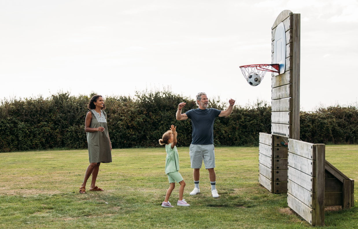A couple with a young girl playing basketball with a football in a sports field