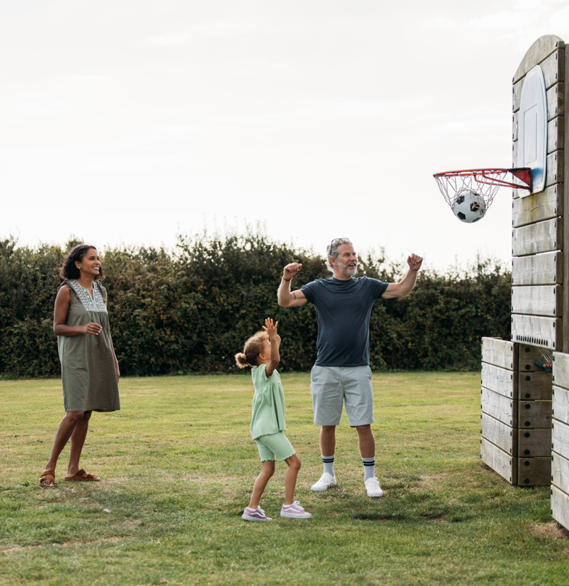 A couple with a young girl playing basketball with a football in a sports field