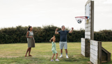 A couple with a young girl playing basketball with a football in a sports field